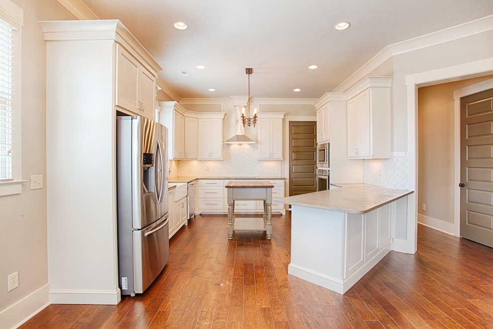 Inspiration for a mid-sized timeless u-shaped medium tone wood floor enclosed kitchen remodel in Other with a farmhouse sink, shaker cabinets, white cabinets, limestone countertops, white backsplash, ceramic backsplash, stainless steel appliances and a peninsula