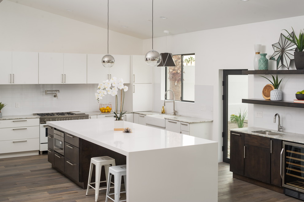 Photo of a contemporary l-shaped kitchen in Phoenix with flat-panel cabinets, an island, a belfast sink, white cabinets, white splashback, glass sheet splashback, stainless steel appliances, light hardwood flooring and beige floors.