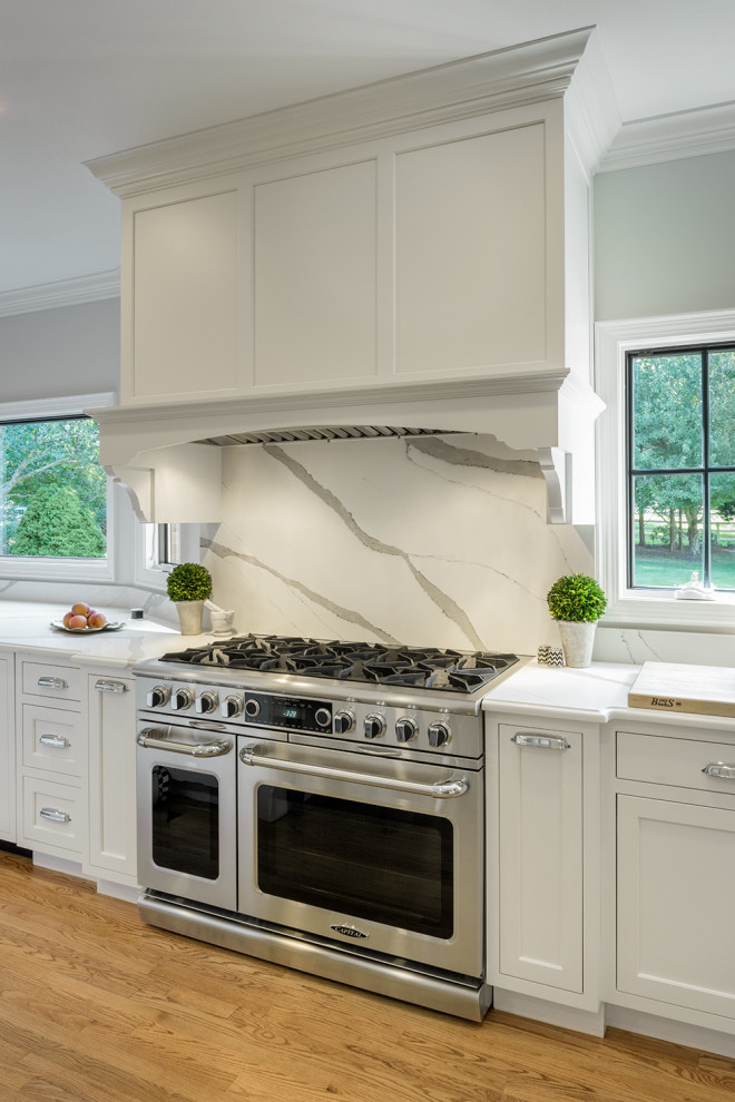 Expansive contemporary galley open plan kitchen in Providence with a single-bowl sink, beaded cabinets, white cabinets, engineered stone countertops, white splashback, stainless steel appliances, light hardwood flooring, an island and white worktops.