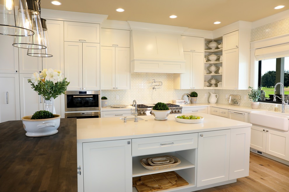 Inspiration for a large country u-shaped open plan kitchen in Portland with a belfast sink, shaker cabinets, white cabinets, engineered stone countertops, green splashback, ceramic splashback, integrated appliances, medium hardwood flooring, an island, beige floors and yellow worktops.
