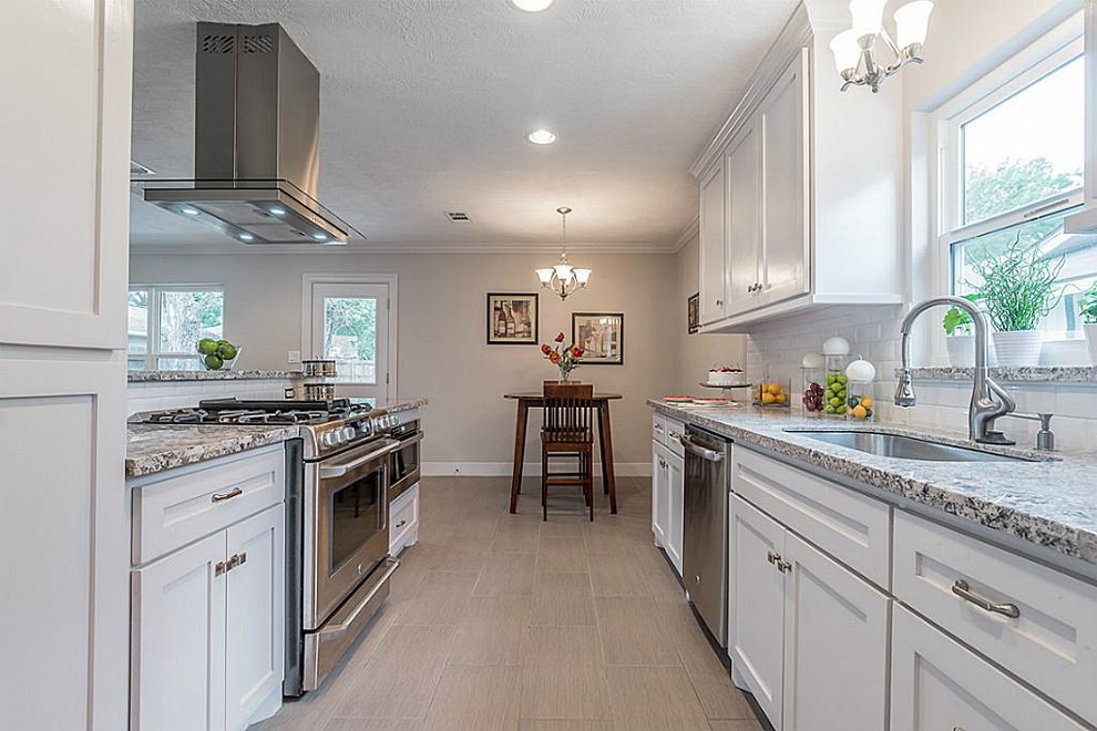 Design ideas for a mid-sized arts and crafts galley open plan kitchen in Houston with a single-bowl sink, shaker cabinets, white cabinets, granite benchtops, white splashback, subway tile splashback, stainless steel appliances, vinyl floors, no island and beige floor.