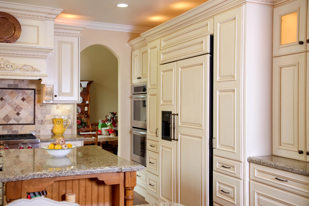 Example of a large classic u-shaped medium tone wood floor eat-in kitchen design in Orange County with a farmhouse sink, recessed-panel cabinets, white cabinets, granite countertops, multicolored backsplash, subway tile backsplash, black appliances and an island