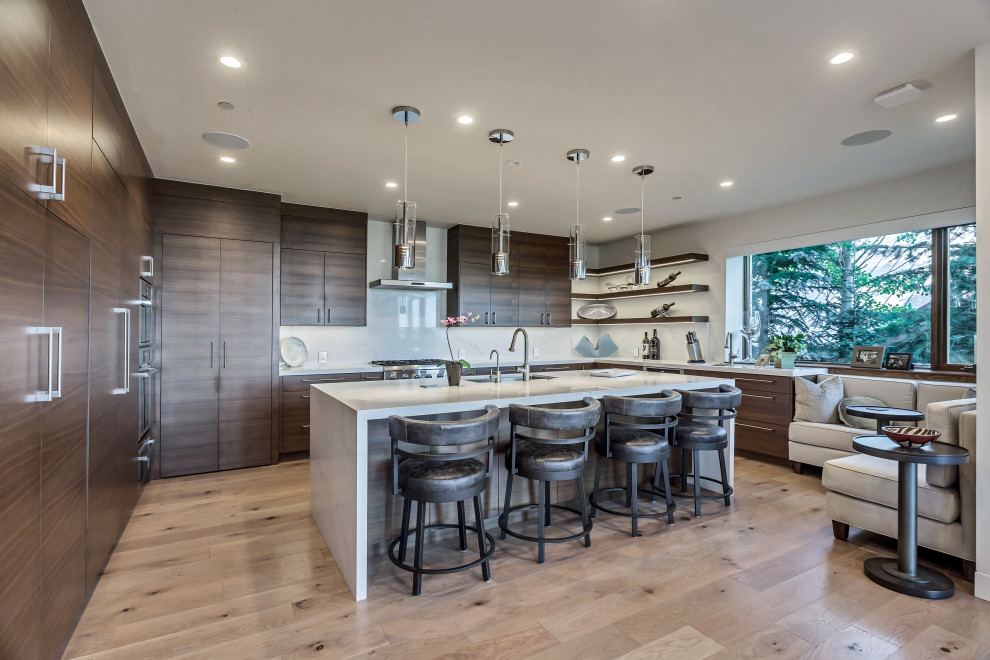 Photo of a contemporary u-shaped kitchen/diner in Salt Lake City with a submerged sink, flat-panel cabinets, medium wood cabinets, white splashback, integrated appliances, medium hardwood flooring, an island, brown floors and white worktops.
