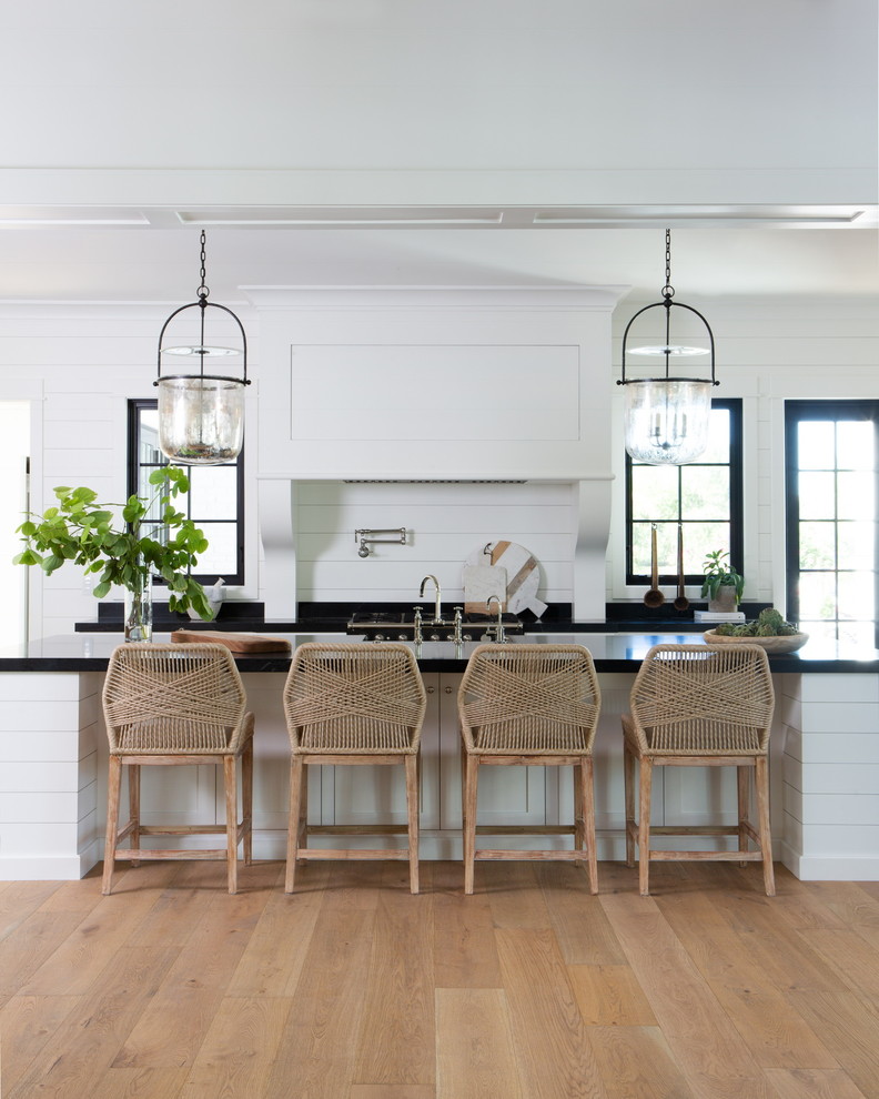 Country galley kitchen in Phoenix with shaker cabinets, white cabinets, soapstone worktops, an island, black worktops, white splashback, wood splashback, medium hardwood flooring and brown floors.