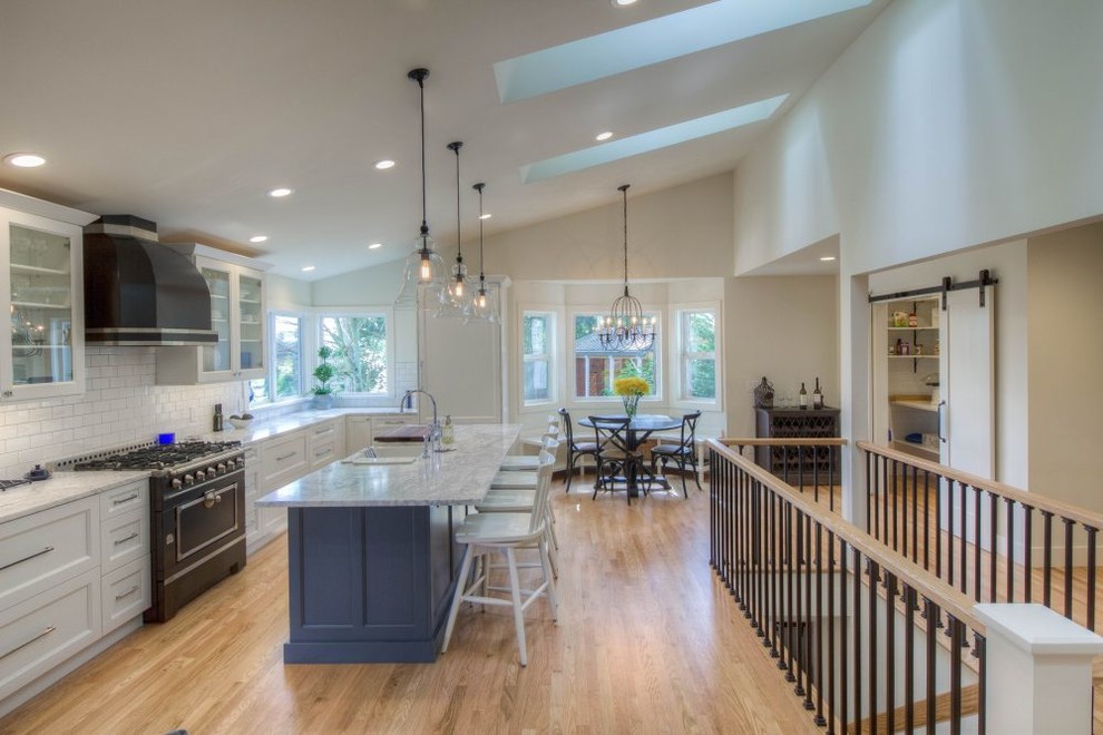 Inspiration for a large transitional u-shaped light wood floor eat-in kitchen remodel in Seattle with a double-bowl sink, raised-panel cabinets, white cabinets, marble countertops, white backsplash, subway tile backsplash, stainless steel appliances and an island