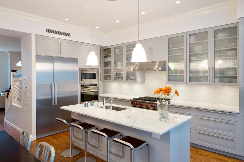 Exempel på ett mellanstort modernt vit vitt kök, med en undermonterad diskho, luckor med glaspanel, grå skåp, bänkskiva i kvarts, vitt stänkskydd, stänkskydd i sten, rostfria vitvaror, mellanmörkt trägolv, en köksö och brunt golv
