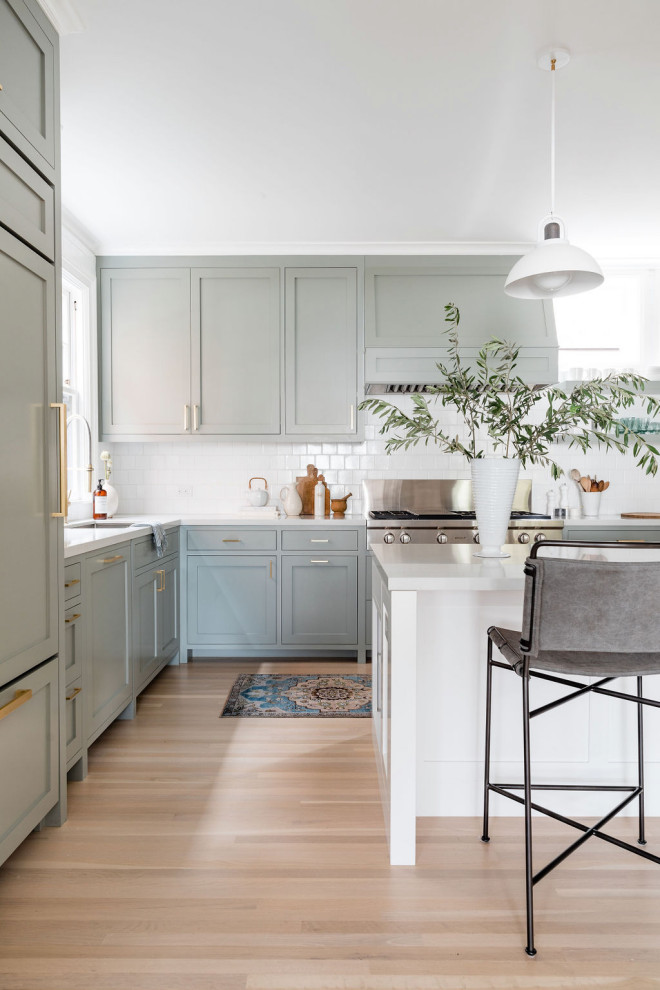 Inspiration for a large transitional l-shaped light wood floor open concept kitchen remodel in San Francisco with an undermount sink, gray cabinets, white backsplash, ceramic backsplash, stainless steel appliances, an island and white countertops