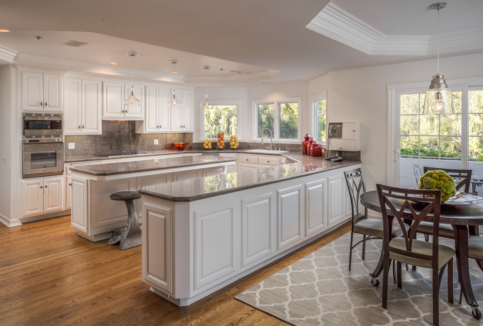 Foto på ett medelhavsstil kök och matrum, med en nedsänkt diskho, luckor med upphöjd panel, vita skåp, grått stänkskydd, rostfria vitvaror, mellanmörkt trägolv och en halv köksö