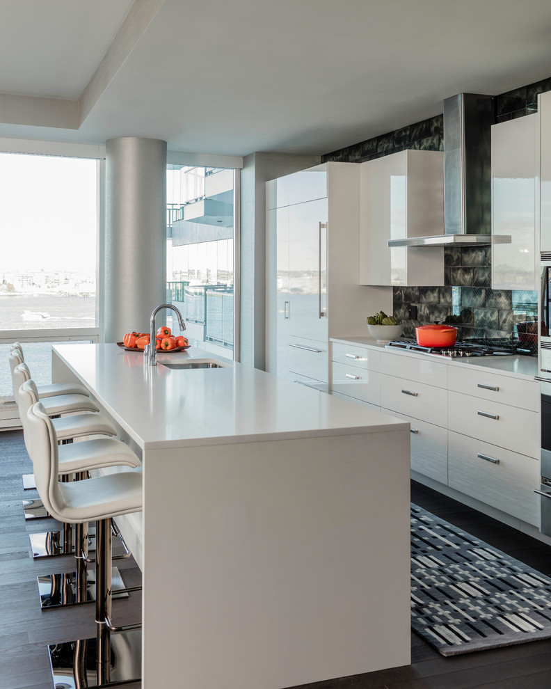 This is an example of a contemporary galley kitchen in Boston with a submerged sink, flat-panel cabinets, white cabinets, black splashback, integrated appliances, dark hardwood flooring, an island, brown floors and white worktops.