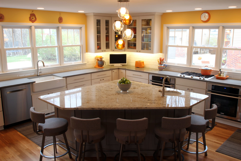 Example of a large transitional l-shaped eat-in kitchen design in Other with a farmhouse sink, shaker cabinets, white cabinets, white backsplash, subway tile backsplash, stainless steel appliances, two islands and solid surface countertops