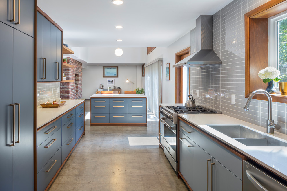Bild på ett mellanstort retro kök, med en undermonterad diskho, släta luckor, blå skåp, bänkskiva i kvarts, grått stänkskydd, stänkskydd i porslinskakel, rostfria vitvaror, betonggolv, en köksö och grått golv