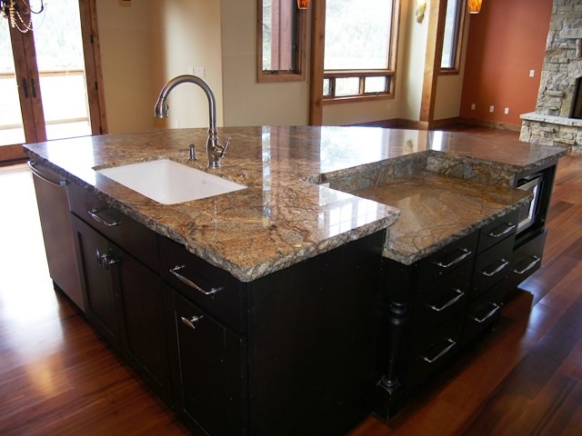 Bild på ett stort rustikt kök och matrum, med en dubbel diskho, släta luckor, skåp i mörkt trä, granitbänkskiva, vitt stänkskydd, stänkskydd i stenkakel, svarta vitvaror, mörkt trägolv och en köksö