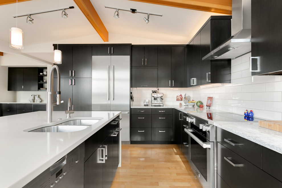 Example of a mid-century modern l-shaped light wood floor and beige floor kitchen design in Seattle with a double-bowl sink, flat-panel cabinets, white backsplash, subway tile backsplash, stainless steel appliances, an island and white countertops