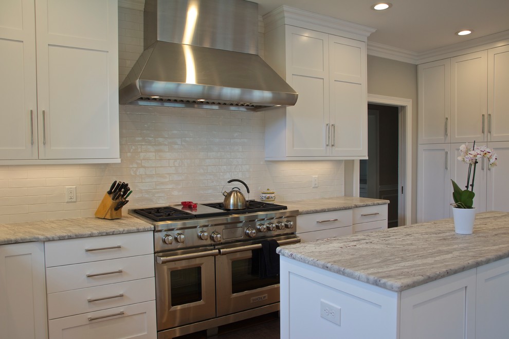 This is an example of a large traditional l-shaped kitchen/diner in Cincinnati with a submerged sink, shaker cabinets, white cabinets, granite worktops, white splashback, ceramic splashback, integrated appliances, medium hardwood flooring, an island and brown floors.