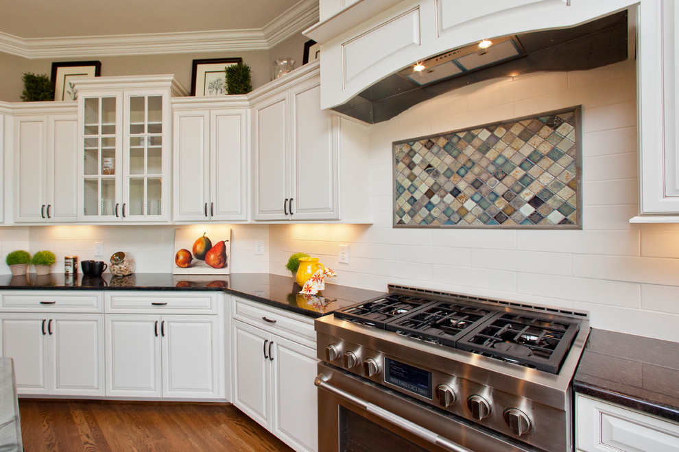 Bild på ett stort vintage kök, med en undermonterad diskho, skåp i shakerstil, vita skåp, granitbänkskiva, vitt stänkskydd, stänkskydd i keramik, rostfria vitvaror, mellanmörkt trägolv och en köksö