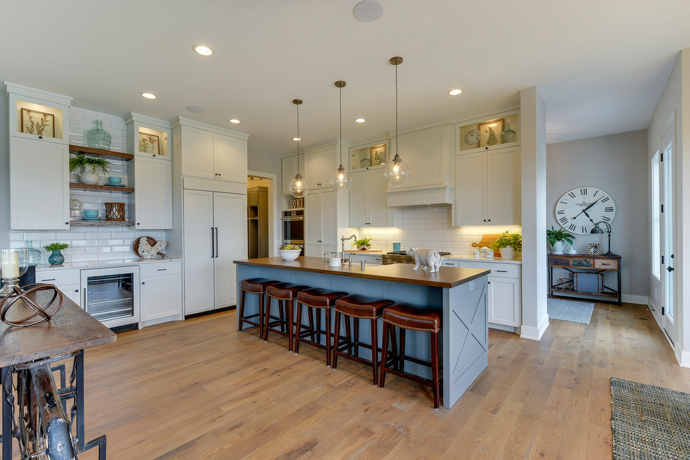 Mid-sized cottage galley medium tone wood floor and brown floor open concept kitchen photo in Minneapolis with a farmhouse sink, shaker cabinets, white cabinets, wood countertops, white backsplash, subway tile backsplash, paneled appliances, an island and brown countertops