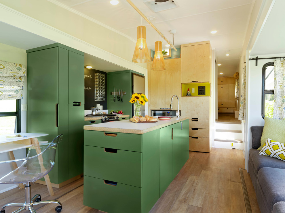 This is an example of a small l-shaped open plan kitchen in Burlington with a built-in sink, flat-panel cabinets, green cabinets, laminate countertops, stainless steel appliances, cork flooring, an island and beige floors.