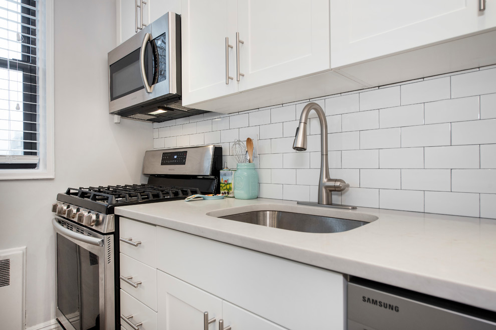 Idéer för ett litet modernt linjärt kök med öppen planlösning, med en undermonterad diskho, luckor med infälld panel, vita skåp, vitt stänkskydd, stänkskydd i tunnelbanekakel, rostfria vitvaror, mellanmörkt trägolv och en köksö
