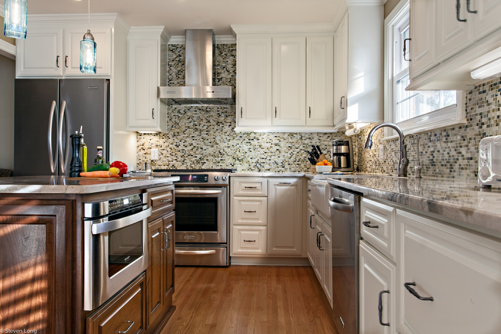 Klassische Wohnküche in L-Form mit Landhausspüle, profilierten Schrankfronten, weißen Schränken, Granit-Arbeitsplatte, bunter Rückwand, Küchengeräten aus Edelstahl, Rückwand aus Mosaikfliesen, braunem Holzboden und Kücheninsel in Nashville