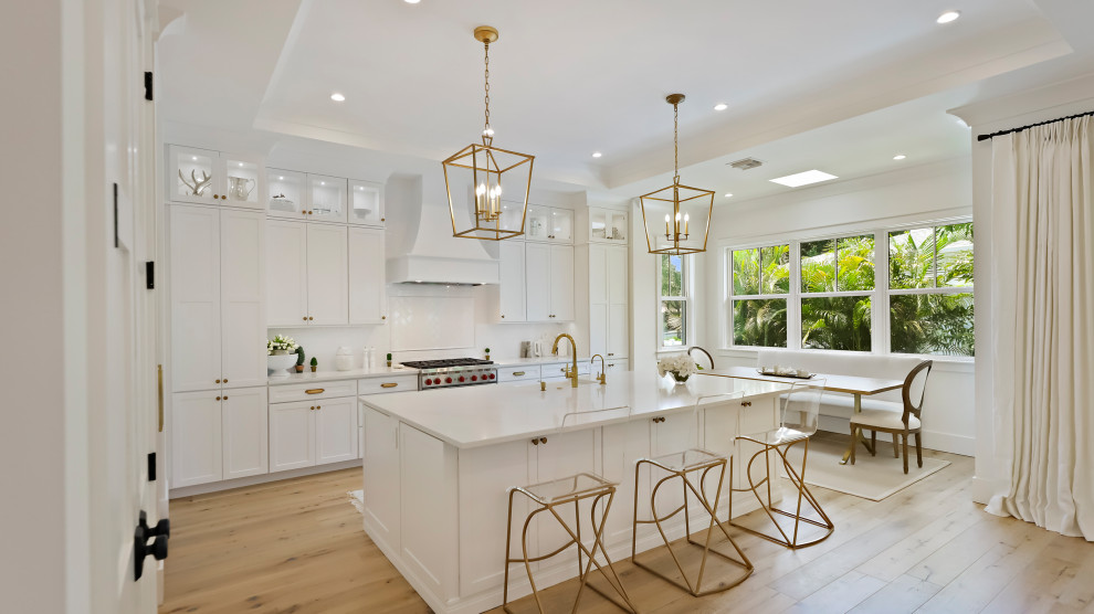 This is an example of a large traditional l-shaped kitchen/diner in Tampa with a built-in sink, shaker cabinets, white cabinets, white splashback, stainless steel appliances, light hardwood flooring, multiple islands, beige floors and beige worktops.