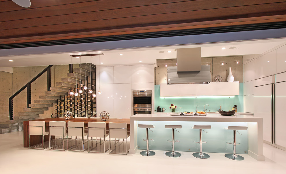 Offene Moderne Küche in U-Form mit flächenbündigen Schrankfronten, weißen Schränken, Küchenrückwand in Blau, Glasrückwand und Elektrogeräten mit Frontblende in Orange County