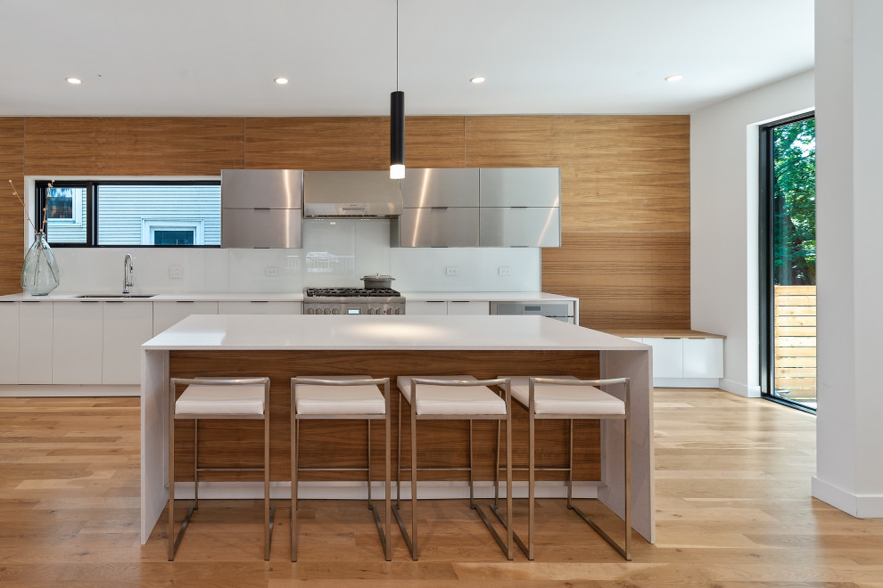 Trendy light wood floor kitchen photo in Chicago with a single-bowl sink, flat-panel cabinets, stainless steel cabinets, solid surface countertops, red backsplash, glass sheet backsplash, stainless steel appliances, an island and white countertops