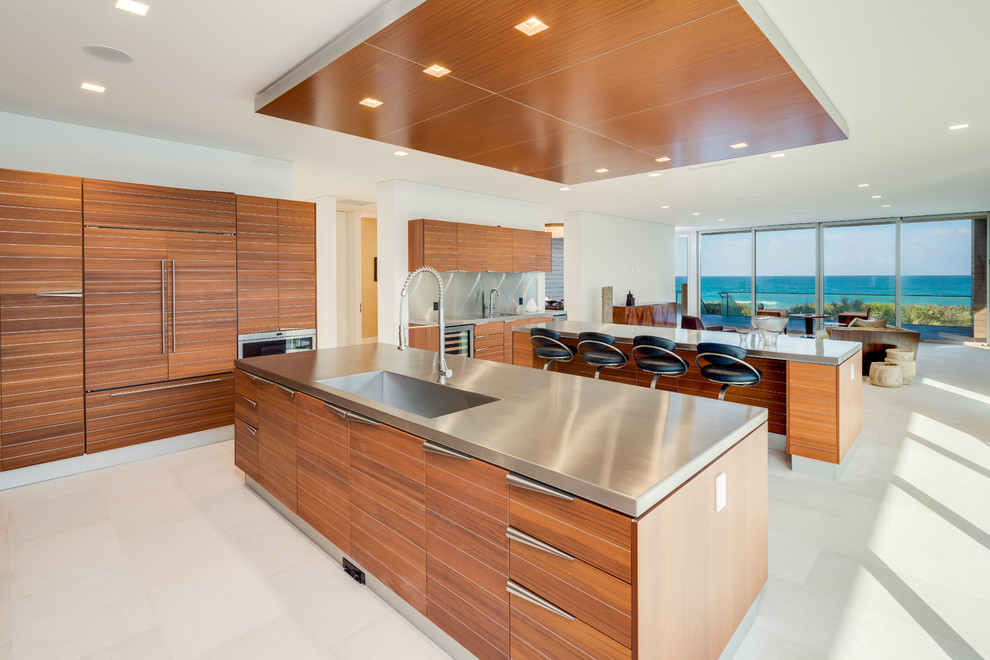 Moderne Küche mit integriertem Waschbecken, flächenbündigen Schrankfronten, hellbraunen Holzschränken, Edelstahl-Arbeitsplatte, Küchenrückwand in Grau, zwei Kücheninseln, weißem Boden und grauer Arbeitsplatte in Miami