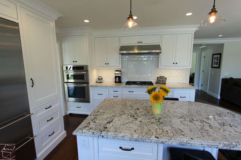 Example of a mid-sized transitional single-wall dark wood floor eat-in kitchen design in Orange County with a double-bowl sink, shaker cabinets, white cabinets, granite countertops, white backsplash, subway tile backsplash, stainless steel appliances and an island