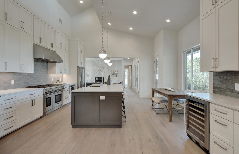 Exemple d'une cuisine moderne avec un placard à porte shaker, des portes de placard blanches, un plan de travail en quartz, une crédence grise, un électroménager en acier inoxydable et un sol en bois brun.