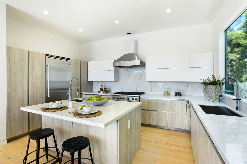 Moderne Küche in L-Form mit Unterbauwaschbecken, flächenbündigen Schrankfronten, hellen Holzschränken, Küchenrückwand in Weiß, Küchengeräten aus Edelstahl, hellem Holzboden und Kücheninsel in Los Angeles