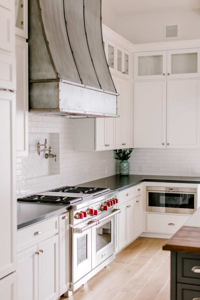 Inspiration for a cottage l-shaped light wood floor open concept kitchen remodel in Phoenix with a farmhouse sink, shaker cabinets, white cabinets, quartz countertops, white backsplash, brick backsplash, stainless steel appliances and an island