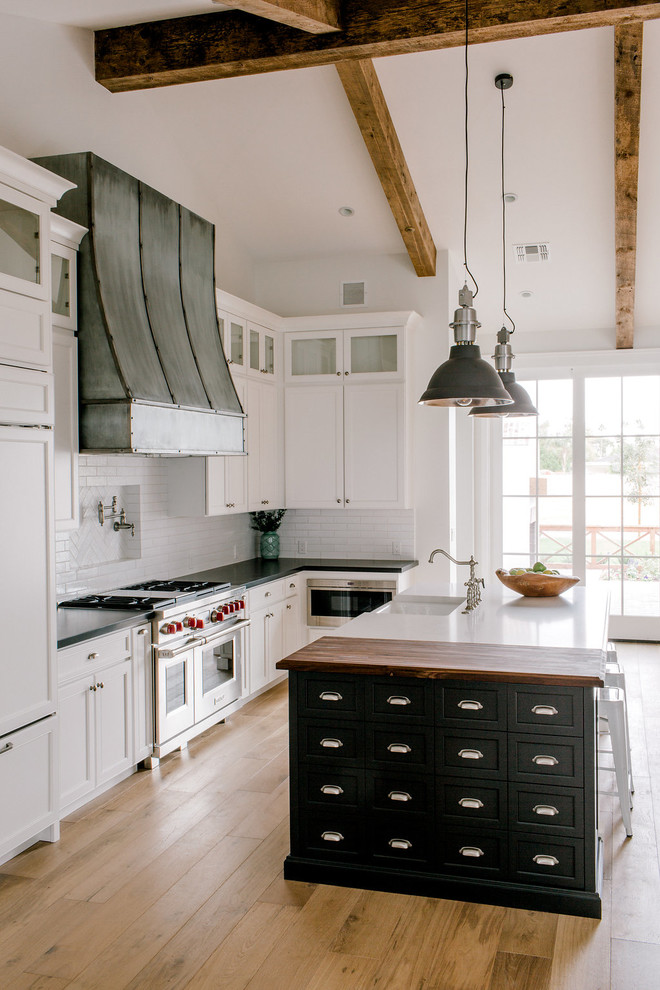 Cottage l-shaped light wood floor open concept kitchen photo in Phoenix with a farmhouse sink, shaker cabinets, white cabinets, quartz countertops, white backsplash, brick backsplash, stainless steel appliances and an island