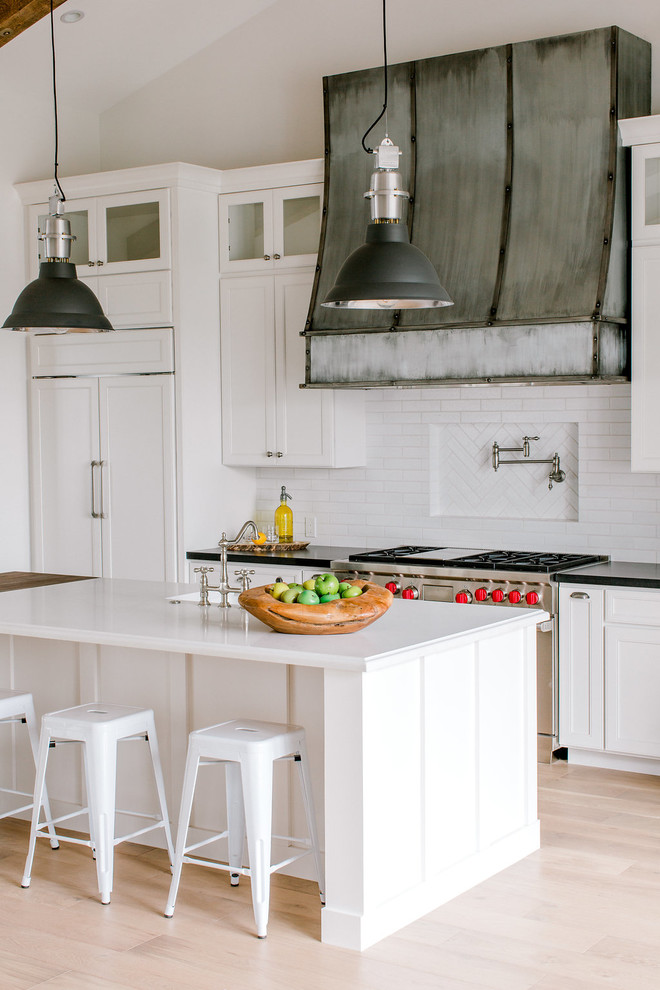 Example of a cottage light wood floor and beige floor kitchen design in Phoenix with an undermount sink, shaker cabinets, white cabinets, white backsplash, paneled appliances, an island and white countertops