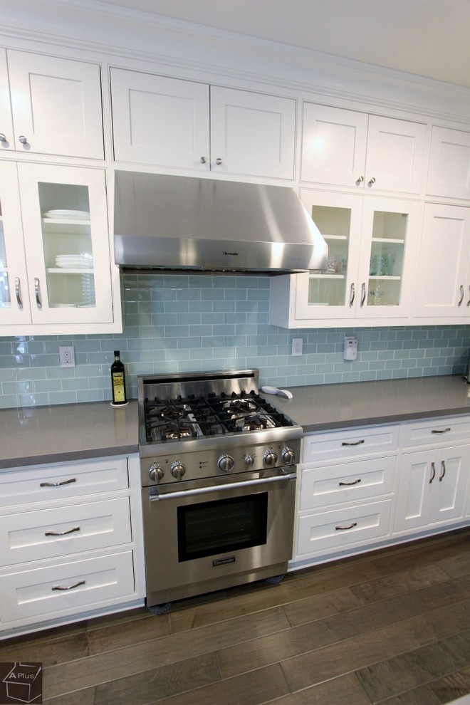 Inredning av ett modernt mellanstort kök, med en rustik diskho, skåp i shakerstil, vita skåp, bänkskiva i kvartsit, blått stänkskydd, stänkskydd i glaskakel, rostfria vitvaror, mellanmörkt trägolv och en köksö