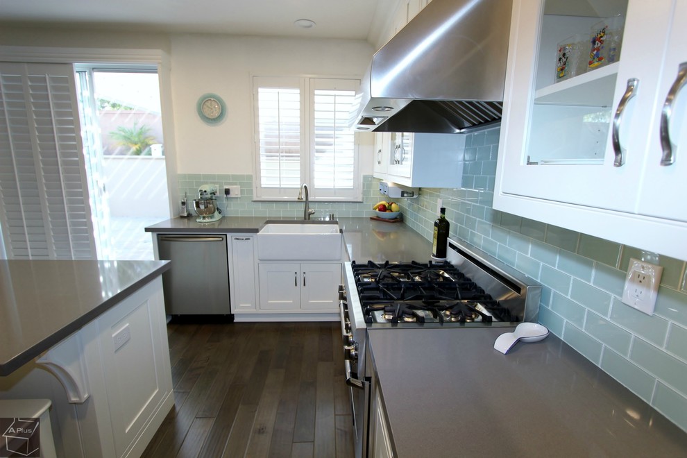 Photo of a medium sized contemporary l-shaped kitchen/diner in Orange County with a belfast sink, shaker cabinets, white cabinets, quartz worktops, blue splashback, glass tiled splashback, stainless steel appliances, medium hardwood flooring and an island.
