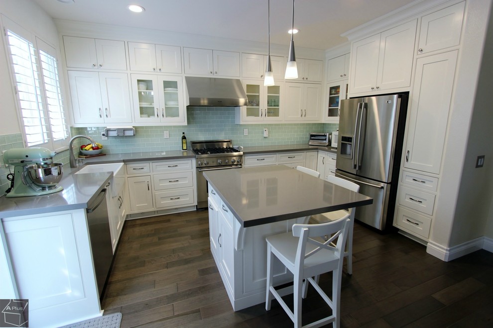Example of a mid-sized trendy l-shaped medium tone wood floor eat-in kitchen design in Orange County with a farmhouse sink, shaker cabinets, white cabinets, quartzite countertops, blue backsplash, glass tile backsplash, stainless steel appliances and an island