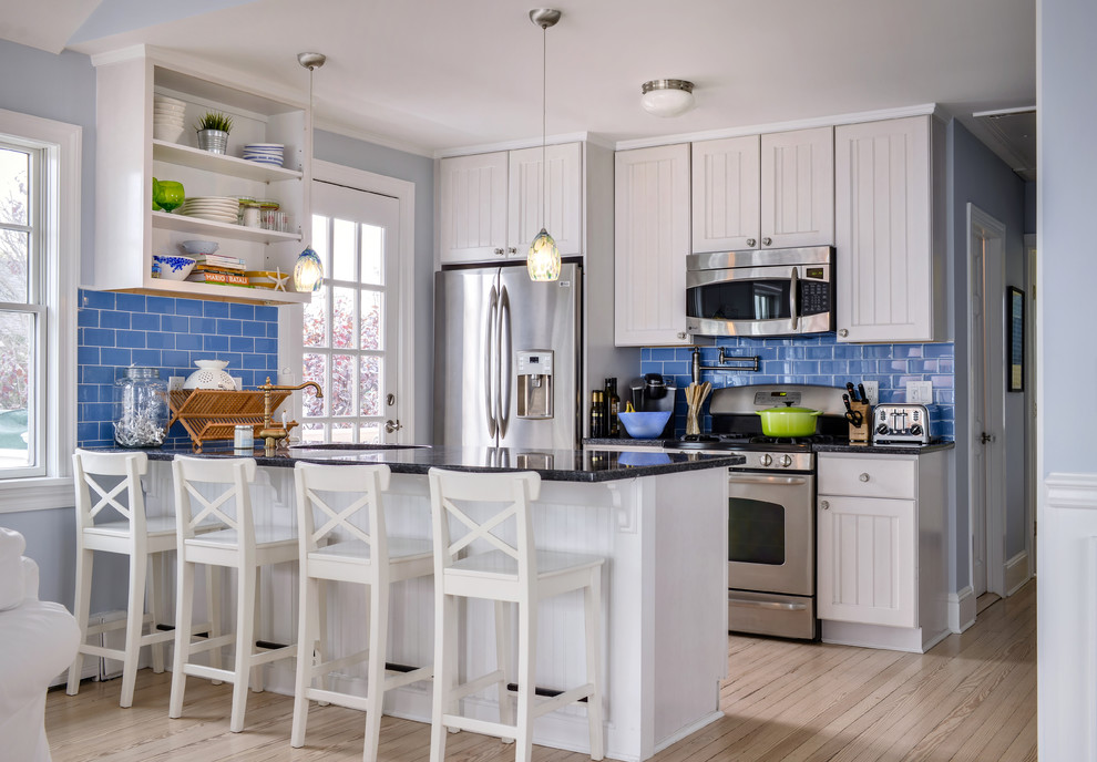 Kitchen - coastal galley light wood floor and beige floor kitchen idea in New York with an undermount sink, white cabinets, granite countertops, stainless steel appliances, black countertops, recessed-panel cabinets, blue backsplash, subway tile backsplash and a peninsula