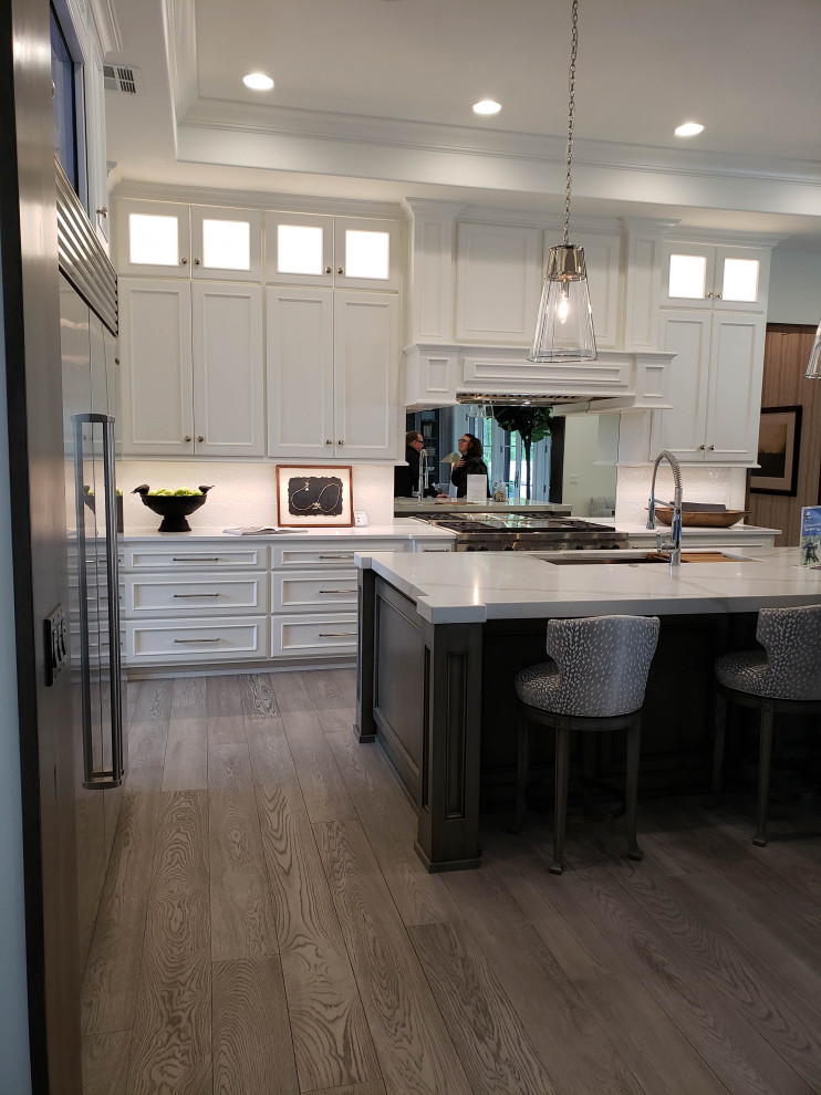 Inspiration for a large mediterranean l-shaped laminate floor, gray floor and tray ceiling eat-in kitchen remodel in Kansas City with an undermount sink, beaded inset cabinets, white cabinets, marble countertops, white backsplash, porcelain backsplash, stainless steel appliances, an island and white countertops