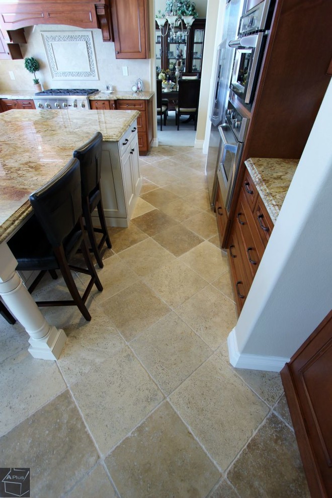 Mid-sized elegant l-shaped porcelain tile eat-in kitchen photo in Orange County with a double-bowl sink, recessed-panel cabinets, medium tone wood cabinets, granite countertops, beige backsplash, stone tile backsplash, stainless steel appliances and an island