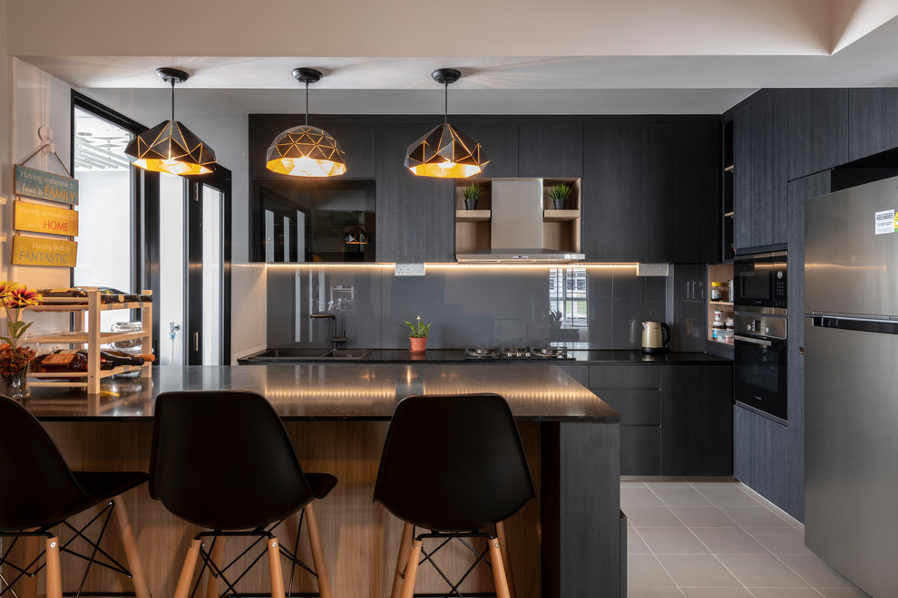 Inspiration for a contemporary l-shaped kitchen in Singapore with a built-in sink, flat-panel cabinets, black cabinets, grey splashback, glass sheet splashback, black appliances, a breakfast bar, beige floors and black worktops.