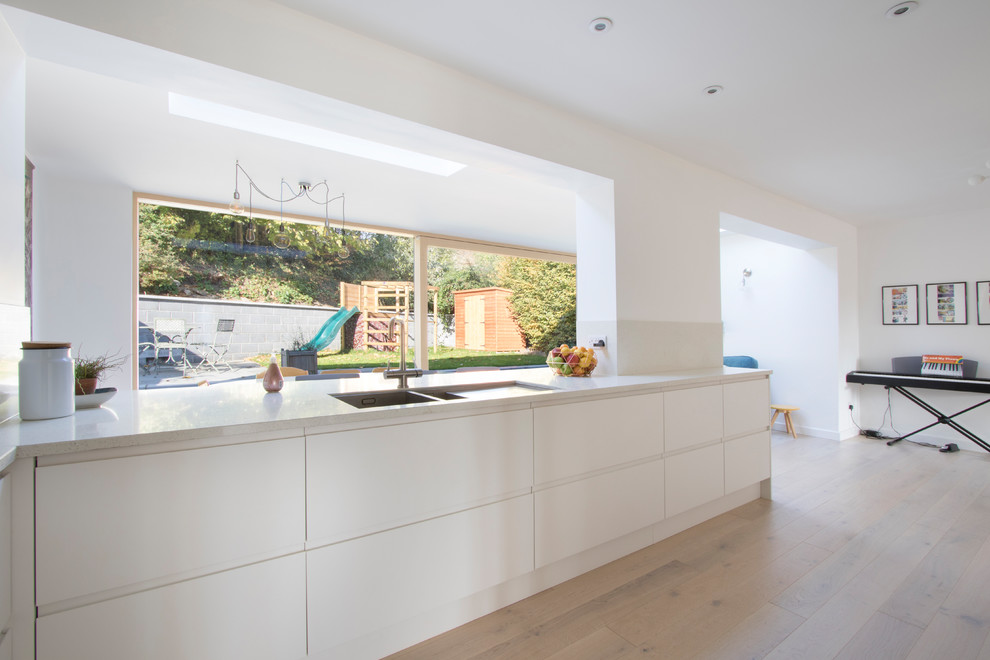Large modern l-shaped open plan kitchen in Gloucestershire with flat-panel cabinets, white cabinets, composite countertops, beige splashback, no island and beige worktops.