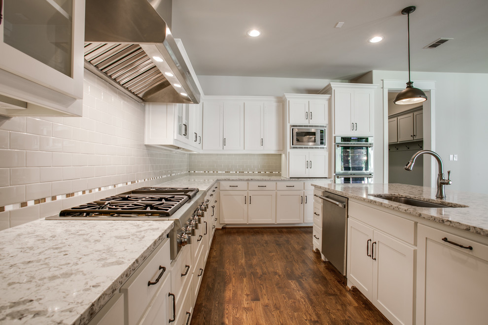 Large classic l-shaped kitchen/diner in Dallas with shaker cabinets, white cabinets, marble worktops, grey splashback, metro tiled splashback, medium hardwood flooring, an island, a submerged sink, stainless steel appliances and brown floors.