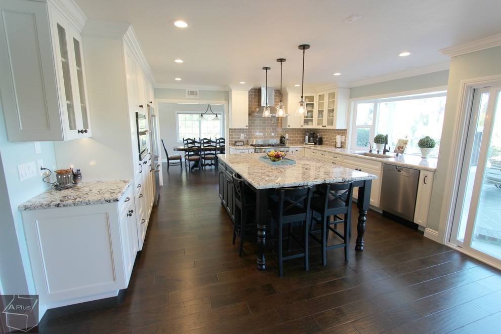 Large elegant l-shaped dark wood floor eat-in kitchen photo in Orange County with a single-bowl sink, recessed-panel cabinets, white cabinets, granite countertops, brown backsplash, subway tile backsplash, stainless steel appliances and an island