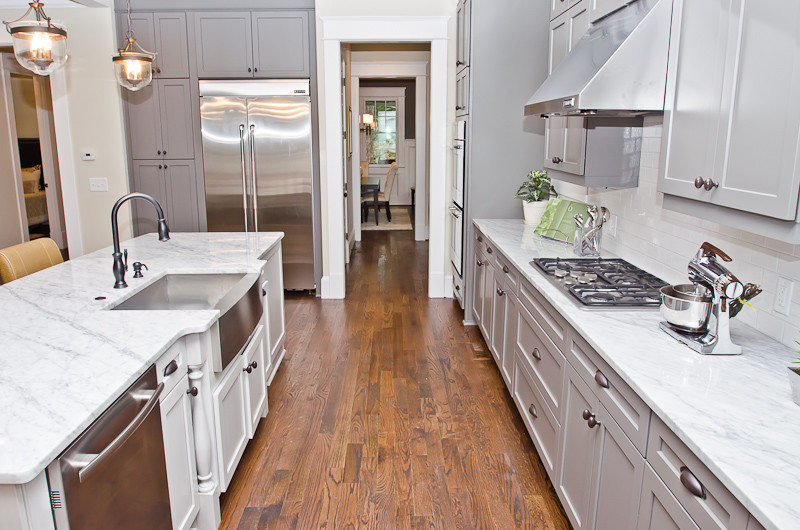 Inspiration for a large craftsman l-shaped medium tone wood floor open concept kitchen remodel in Atlanta with a farmhouse sink, recessed-panel cabinets, gray cabinets, marble countertops, white backsplash, stone tile backsplash, stainless steel appliances and an island