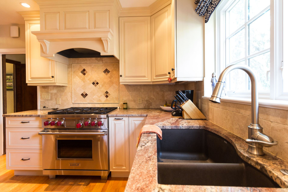 Foto på ett stort vintage kök, med luckor med upphöjd panel, granitbänkskiva, beige stänkskydd, stänkskydd i stenkakel, rostfria vitvaror, mellanmörkt trägolv, brunt golv, en undermonterad diskho, beige skåp och en köksö