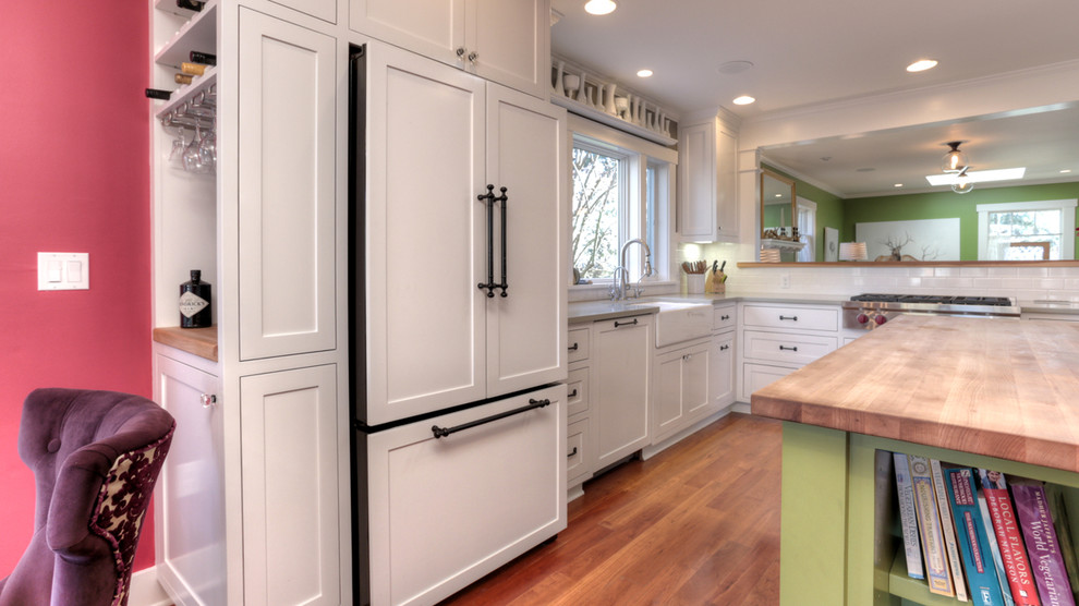 Urige Wohnküche in L-Form mit Landhausspüle, Schrankfronten im Shaker-Stil, weißen Schränken, Küchenrückwand in Weiß, braunem Holzboden und Kücheninsel in Sonstige