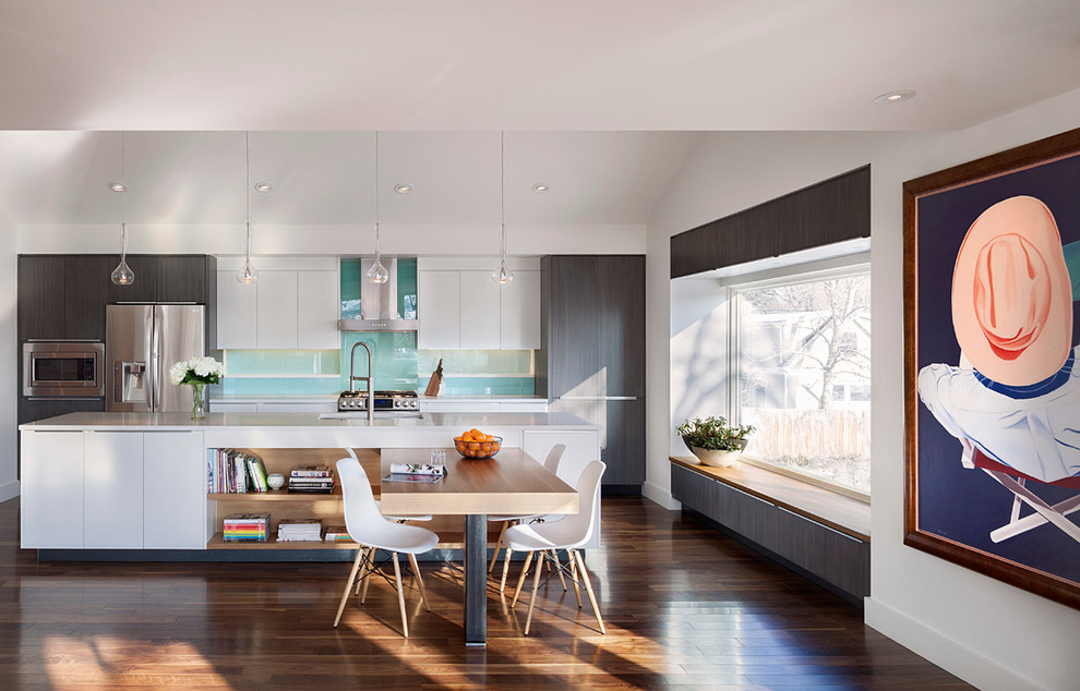Bild på ett funkis kök, med en undermonterad diskho, släta luckor, vita skåp, blått stänkskydd, glaspanel som stänkskydd, rostfria vitvaror, mellanmörkt trägolv och en köksö