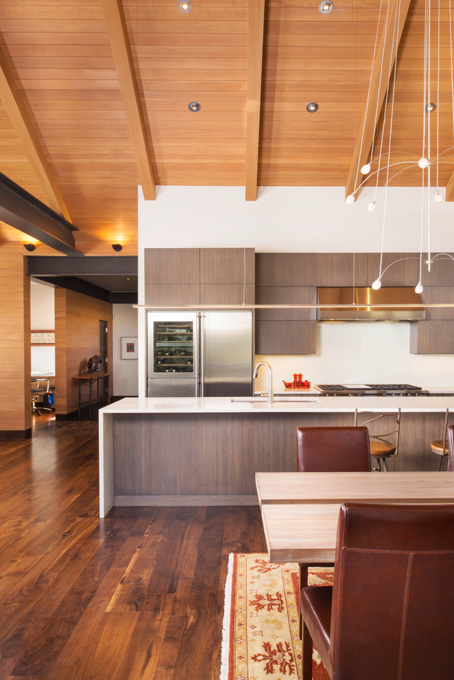 This is an example of a large contemporary single-wall open plan kitchen in Denver with flat-panel cabinets, dark wood cabinets, stainless steel appliances, medium hardwood flooring, an island, a submerged sink, marble worktops and brown floors.