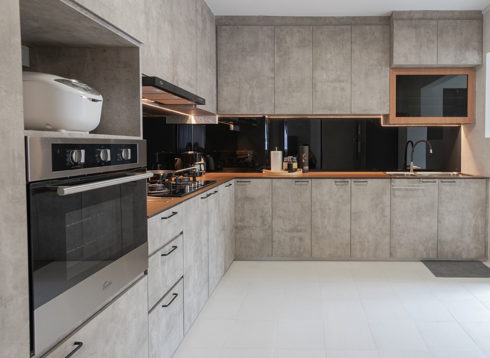 シンガポールにあるコンテンポラリースタイルのおしゃれなL型キッチン (ドロップインシンク、フラットパネル扉のキャビネット、グレーのキャビネット、木材カウンター、黒いキッチンパネル、ガラス板のキッチンパネル、グレーの床、茶色いキッチンカウンター、グレーと黒) の写真