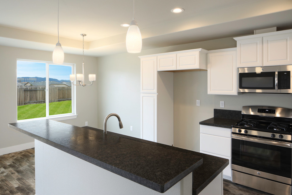 Foto på ett litet funkis kök, med en undermonterad diskho, luckor med upphöjd panel, vita skåp, granitbänkskiva, rostfria vitvaror, mellanmörkt trägolv, en köksö och brunt golv